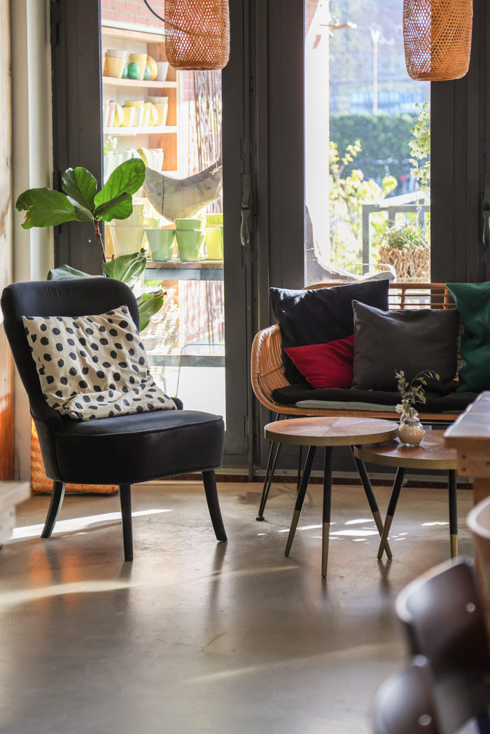 Sessel und Bank mit vielen Kissen drauf und zwei Tischchen stehen vor dem Fenster im Cafe im Kardamom in Münster.