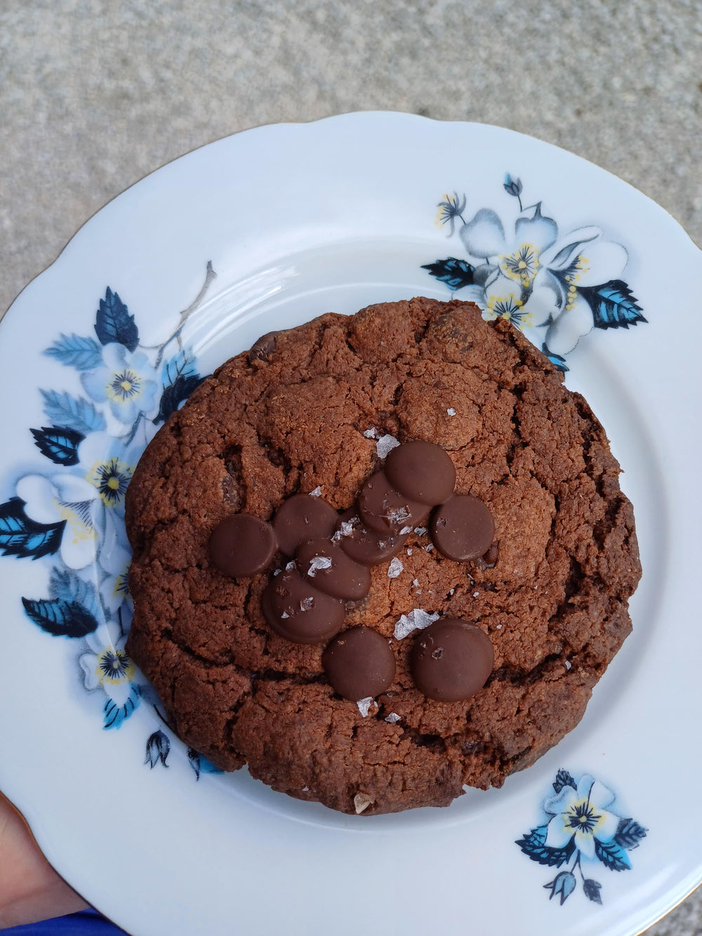 Ein glutenfreier Schokocookie auf einem weißen Teller mit blauen Blümchen. 